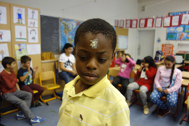 Das Foto zeigt einen Jungen in einem Klassenraum; er hat einen weien Fleck auf die Stirn gemalt. Im Hintergrund sitzen weitere Schüler.