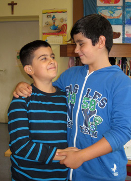 Das Foto zeigt zwei Jungen, die Arm in Arm nebeneinander stehen und sich ansehen.