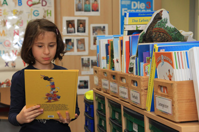 Das Foto zeigt ein Mädchen mit einem Buch, das sie sich gerade aus einem Regal in ihrem Klassenraum genommen hat.