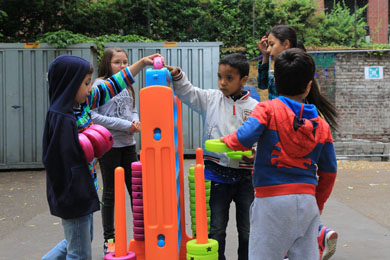 Das Foto zeigt einige Kinder, die auf dem Schulhof ihrer Schule mit einem großen Spiel spielen.