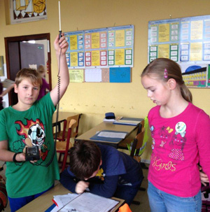 Das Foto zeigt zweit Kinder, welche in einem Klassenraum die Raumtemperatur messen.