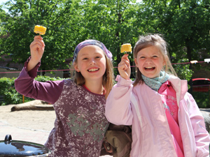 Das Foto zeigt zwei Mädchen, die gedünstete Maisscheiben halten und sich sehr darber freuen.