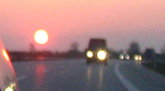 Das Foto zeigt eine regennasse Autobahn mit Autos, dahinter die Abendsonne - aufgenommen im Rckspiegel eines Autos.