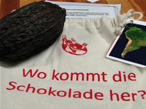 Das Foto zeigt eine Kakaofrucht, diese liegt auf einem Stoffbeutel mit der Aufschrift: Wo kommt die Schokolade her? An dem Stoffbeutel ist ein Satellitenbild von Sdamerika befestigt.