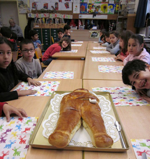 Das Foto zeigt Kinder, die an einem langen Tisch sitzen. Auf dem Tisch liegt ein Weckmann aus Hefeteig.