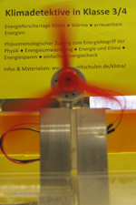 Das Foto zeigt ein thermoelektrisches Element, das aus einem Temperaturgefälle zwischen zwei Wassertanks elektrischen Strom erzeugt und damit einen Motor mit Propeller antreibt. Diese Aktion der Klimadetektive auf der MNU-Tagung in Bremerhaven verdeutlicht, dass Wärme eine nutzbare und wertvolle Energieform ist.