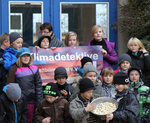 Das Foto zeigt Schüler der Grundschule Damshagen vor ihrer Schule. Sie halten ein Banner, auf dem Klimadetektive steht. Einige Schüler im Vordergrund halten eine Schüssel mit Popcorn, das am ersten Klimadetektive-Projekttag zubereitet wurde.
