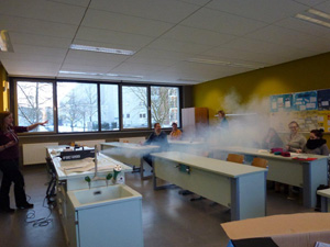 Das Foto zeigt einen Klassenraum mit Schülern. Der Raum wird mittels einer Nebelmaschine eingenebelt.