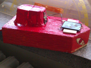 Das Foto zeigt ein kleines rotes Bootsmodell, das mit einer Solarzelle und einem Elektromotor ausgestattet ist.