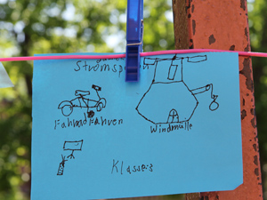 Das Foto zeigt einen blauen Zettel, der an einer Wäscheleine hängt. Auf den Zettel hat ein Schüler drei Klimaschutzideen aufgemalt: Fahrradfahren, Stromsparen und Windmühle.