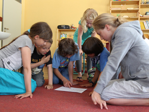 Das Foto zeigt sechs SchülerInnen, die auf einem roten Teppich knien und ein Diagramm betrachten.