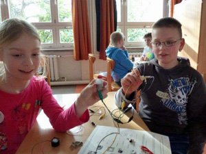 Das Foto zeigt ein Mädchen und einen Jungen, die einen elektrischen Stromkreis gebastelt haben.