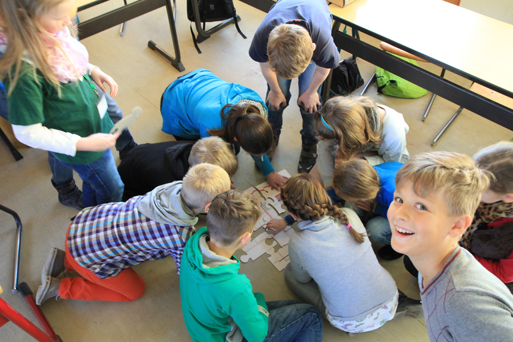 Das Foto zeigt SchülerInnen, die auf dem Fußboden ihres Klassenraums knien und ein Puzzle puzzlen.