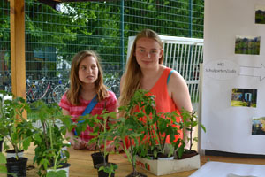 Das Foto zeigt einen Infostand mit zwei Mädchen, im Vordergrund diverse Pflanzen in Blumentöpfen.