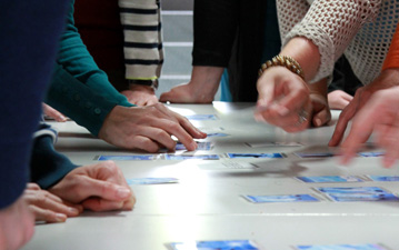 Das Foto zeigt eine Tischplatte und die Hände mehrerer Menschen, die auf dem Tisch Kärtchen sortieren.