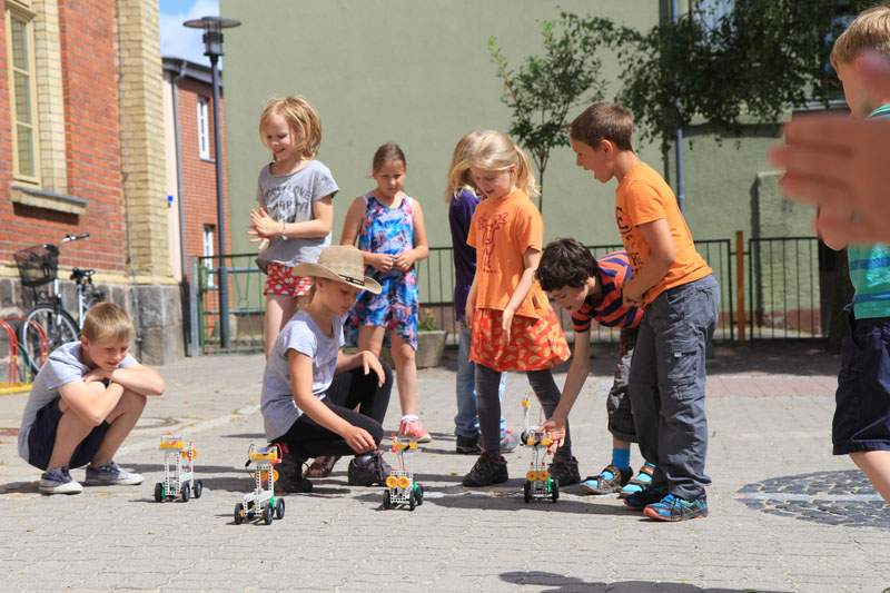 Das Foto zeigt Kinder auf einem sonnigen Schulhof, die mit Solarautos spielen.