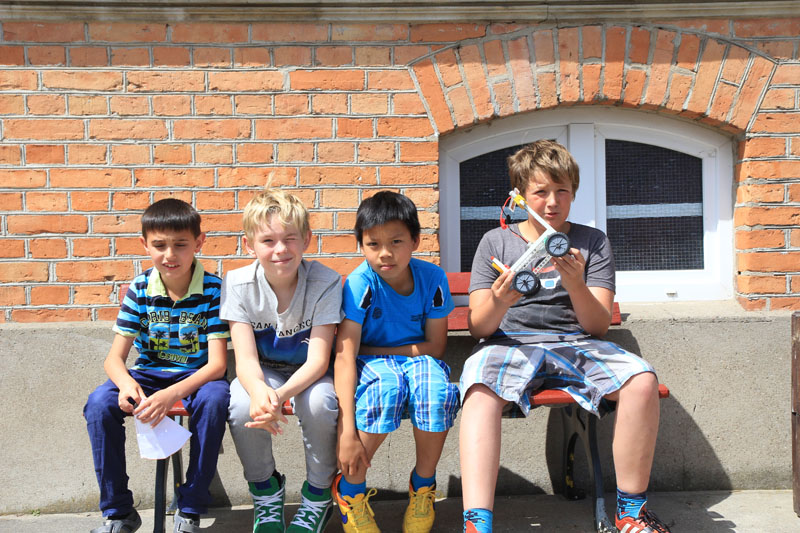 Das Foto zeigt einige Schüler, die auf einem sonnigen Schulhof ihr Solarfahrzeug präsentieren.