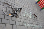 Das Foto zeigt Einzelteile eines Fahrrades, die auf einem Boden aus Betonplatten liegen. Ein Fahrradrahmen ist mit Kreide auf den Boden gezeichnet, daneben der Schriftzug Fahrradpuzzle.