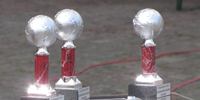 Das Foto zeigt vier Pokale, die jeweils eine silberne Erdkugel tragen.