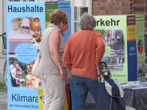 Rentnerinnen betrachten mannsgroße Quader, die mit Informationen zu den Quellen der CO2-Emissionen der Hansestadt Stralsund beschriftet sind. Die Quader sind unterschiedlich groß, ihr Volumen steht für den Anteil der jeweiligen Quelle an den Emissionen.