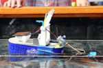 Das Foto zeigt ein kleines Boot, das aus einer Fischkonserve gebaut wurde und mit einer Solarzelle, einem Motor und einer Schiffsschraube als Antrieb ausgestattet ist.