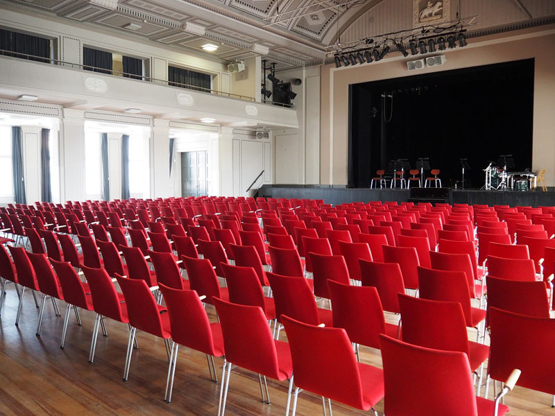 Das Foto zeigt die Stadthalle Greifswald von innen - einen großen Saal mit roten Stühlen.