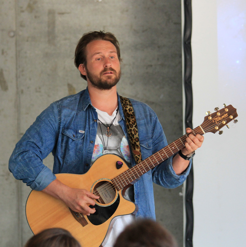 Das Foto zeigt einen singenden Mann mit Gitarre.