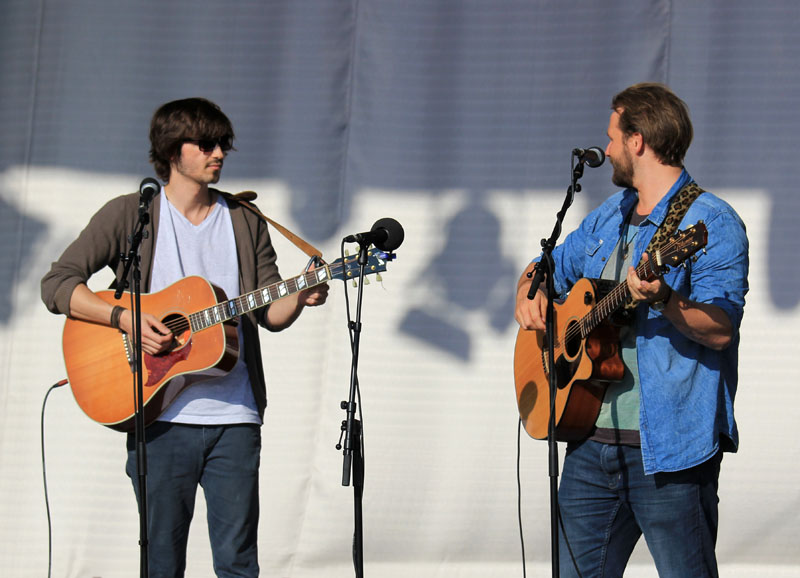 Das Foto zeigt zwei Männer, die auf einer Bühne stehen, singen und dazu Gitarre spielen.