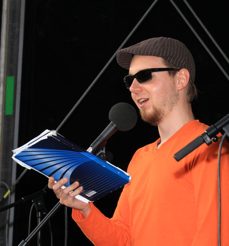 Das Foto zeigt einen Mann, der in ein Mikrofonen spricht.