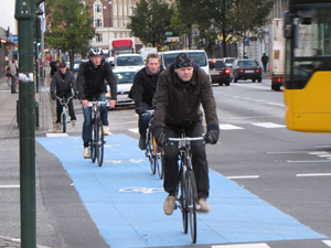 Das Foto zeigt einen kräftig blau eingefärbten Radweg an einer stark befahrenen Straßenkreuzung.