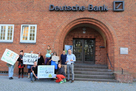 Das Foto zeigt zehn Menschen, die vor der Deutschan Bank Stralsund stehen und mit Transparenten das Ende der fossilen Energien fordern.